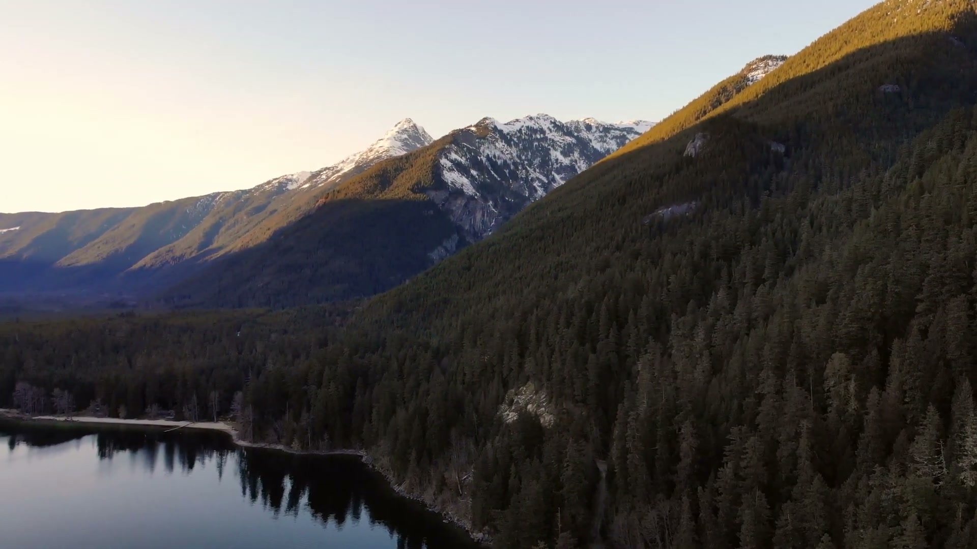 Sunlit forested mountainside above Chilliwack Lake, filmed by drone